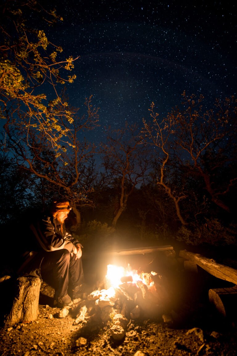 Man near the burning bonfire in the night under a starry sky