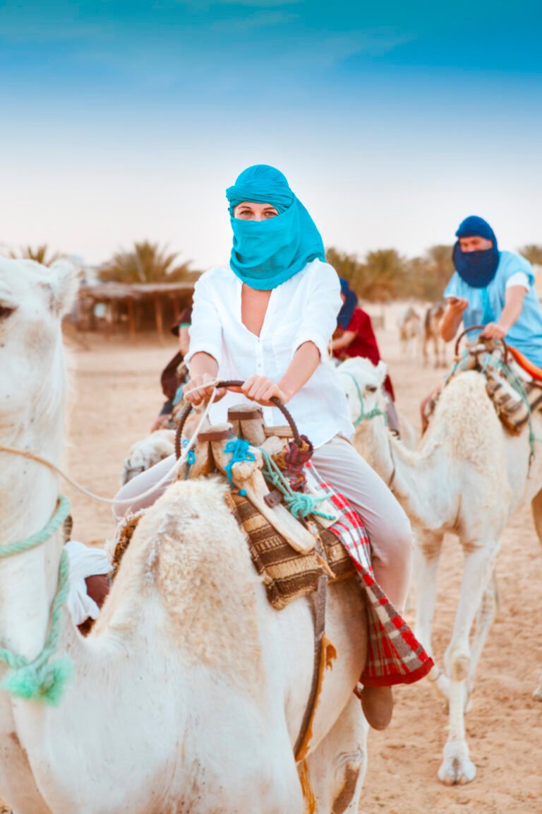 Young caucasian woman tourist riding on camel in sahara desert